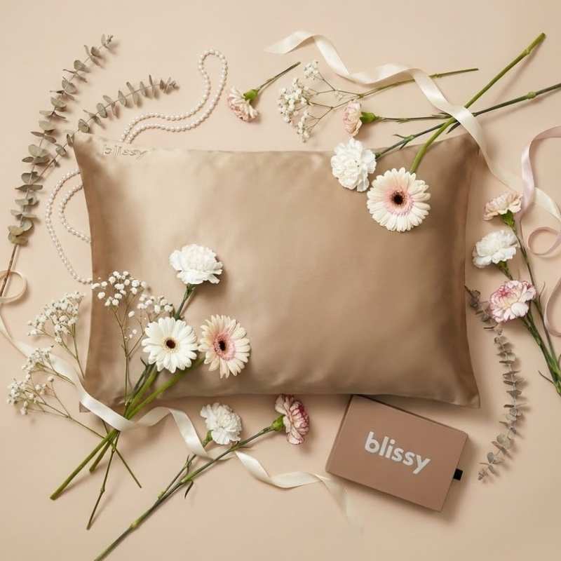 Blissy mulberry silk pillowcase in pink with Blissy gift box on a silk draped surface with flowers