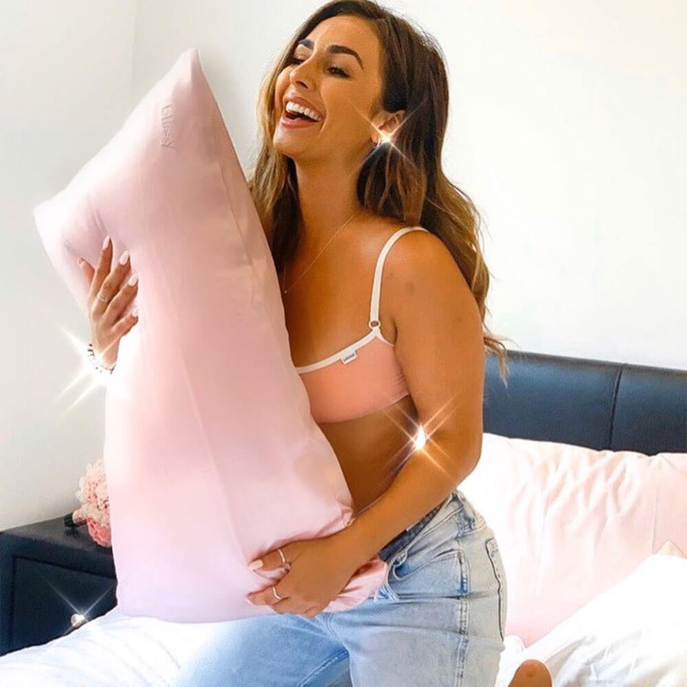 Woman smiling while hugging a pillow with Blissy mulberry silk pink pillowcase